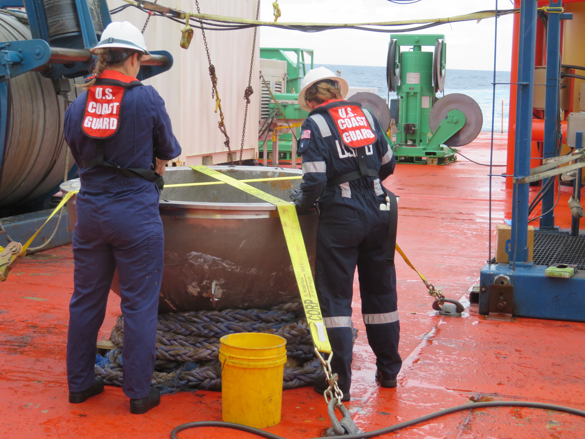 Two US Coast Guard marine safety engineers examining Titan’s recovered titanium endcap on a ship’s deck